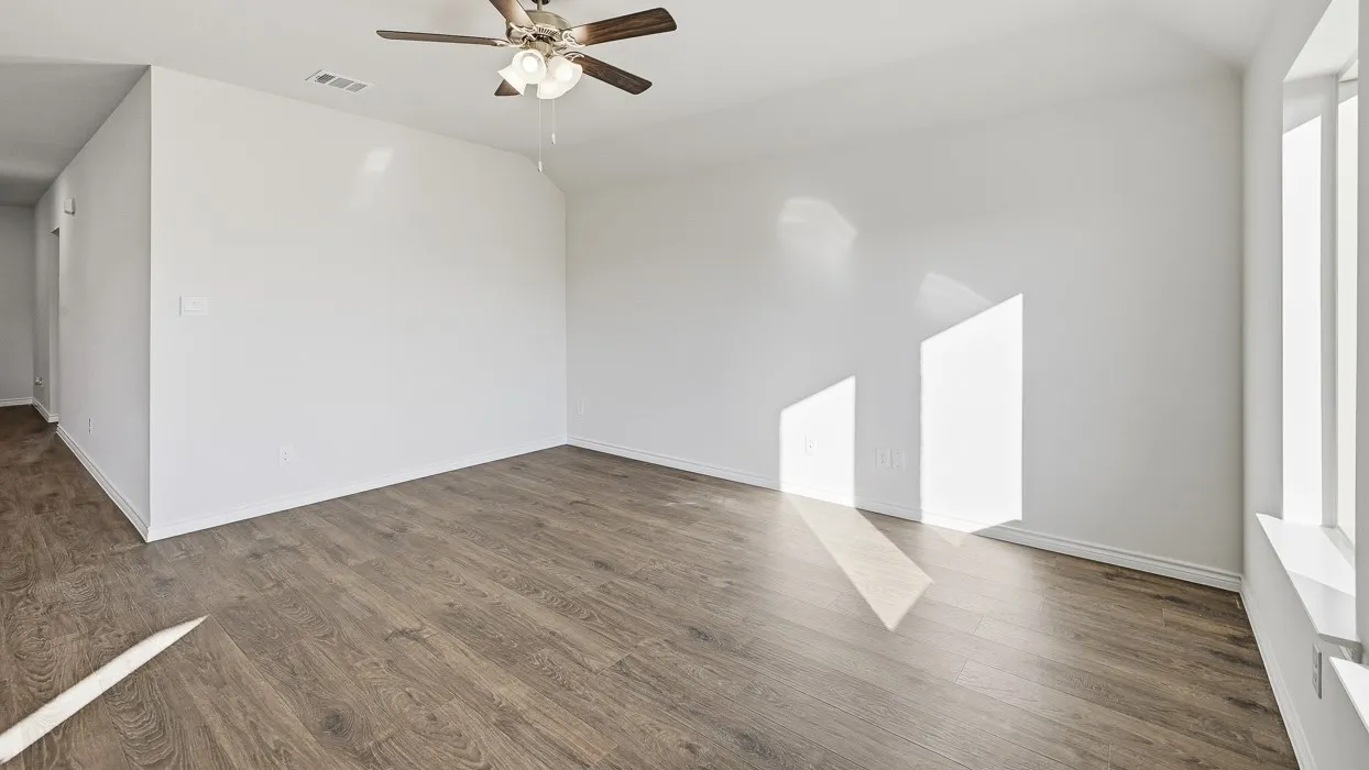 Spacious room featuring wood-finish flooring, white walls, and a ceiling fan with integrated lighting