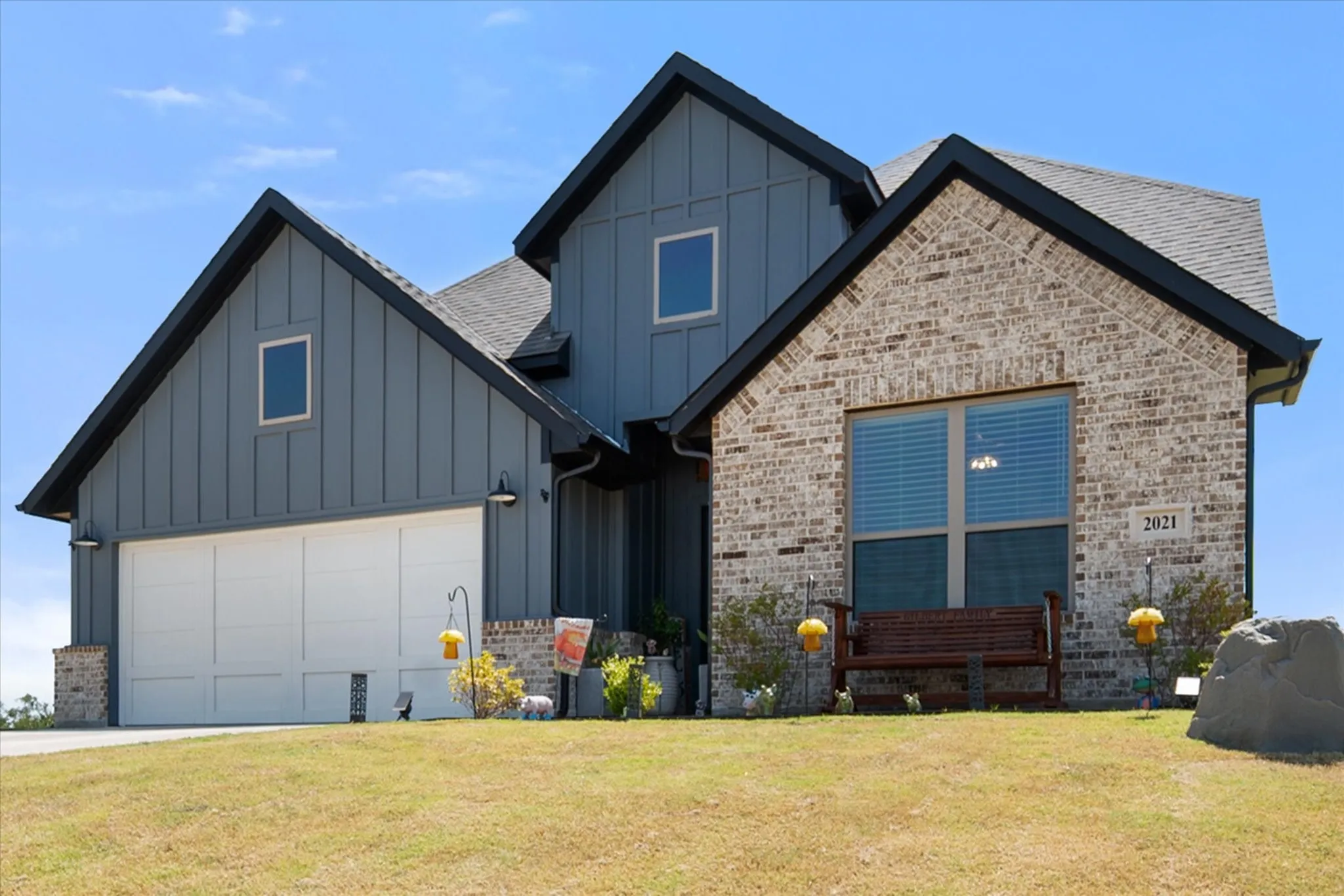 Exterior featuring brick veneer, vertical siding, a white garage door, and a prominent front window