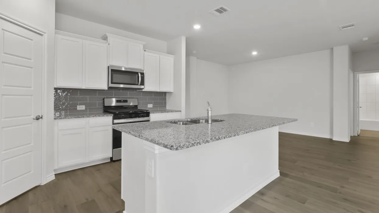 Kitchen featuring white cabinetry, granite countertops, a subway tile backsplash, stainless steel appliances, and a central island with an integrated sink