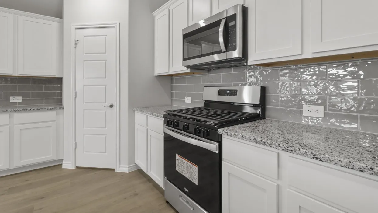 White cabinetry with stainless steel hardware, gray subway tile backsplash, white granite countertops, wood-finish flooring, and a stainless steel gas range with an overhead microwave