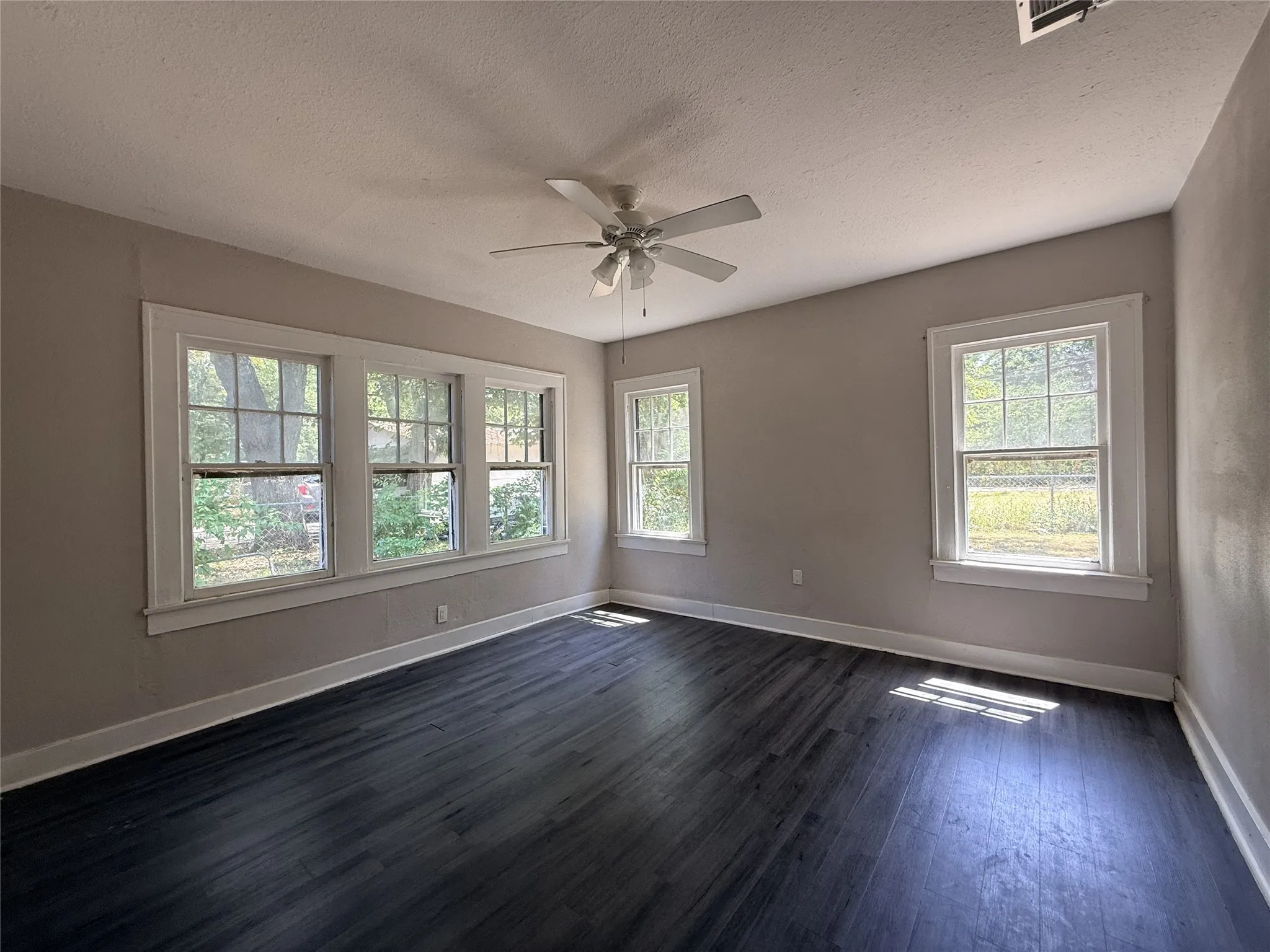 Spacious room with dark wood-finish flooring, multiple windows, and a ceiling fan