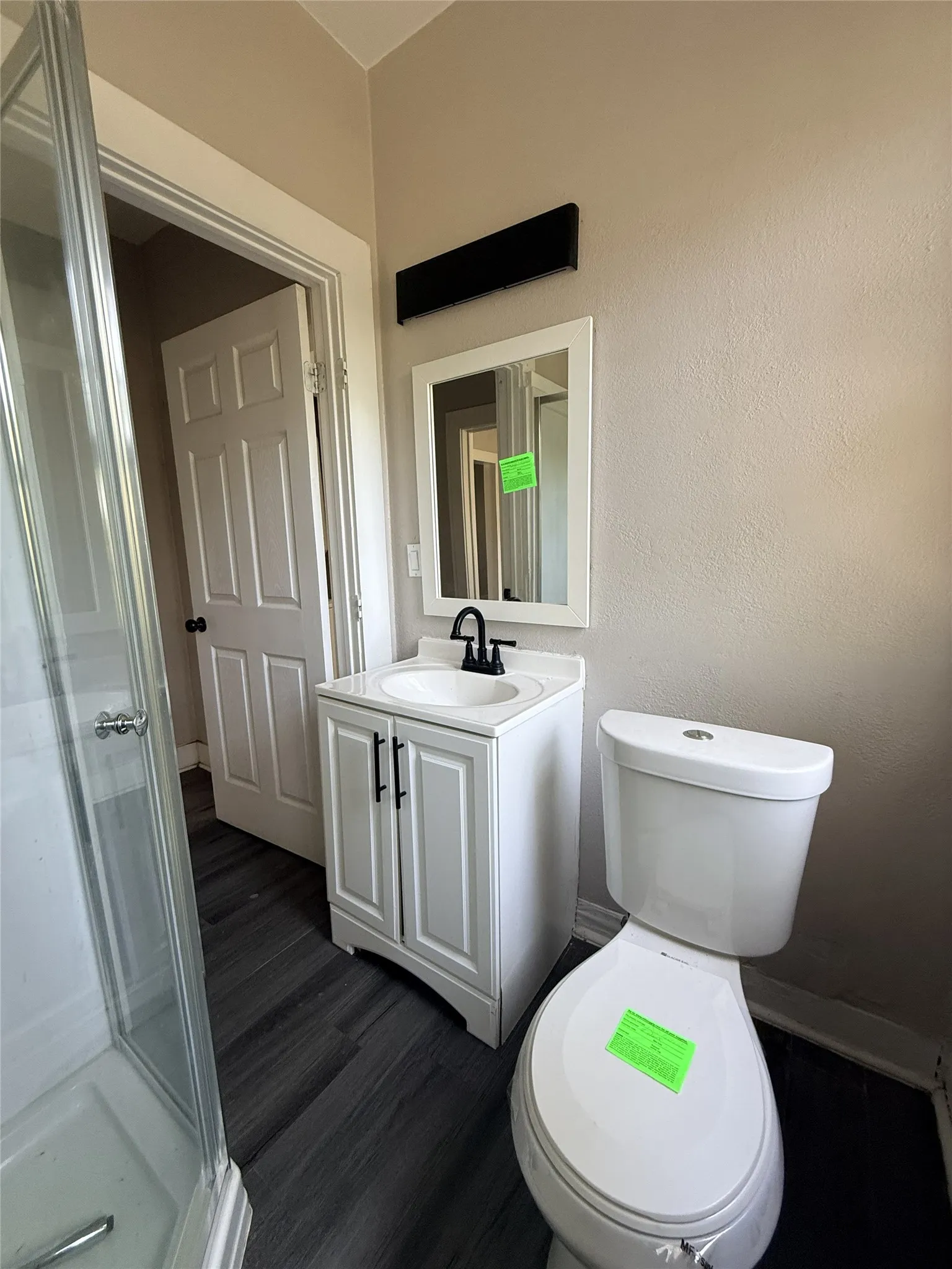 White vanity with a black faucet, framed mirror, and wood-finish flooring