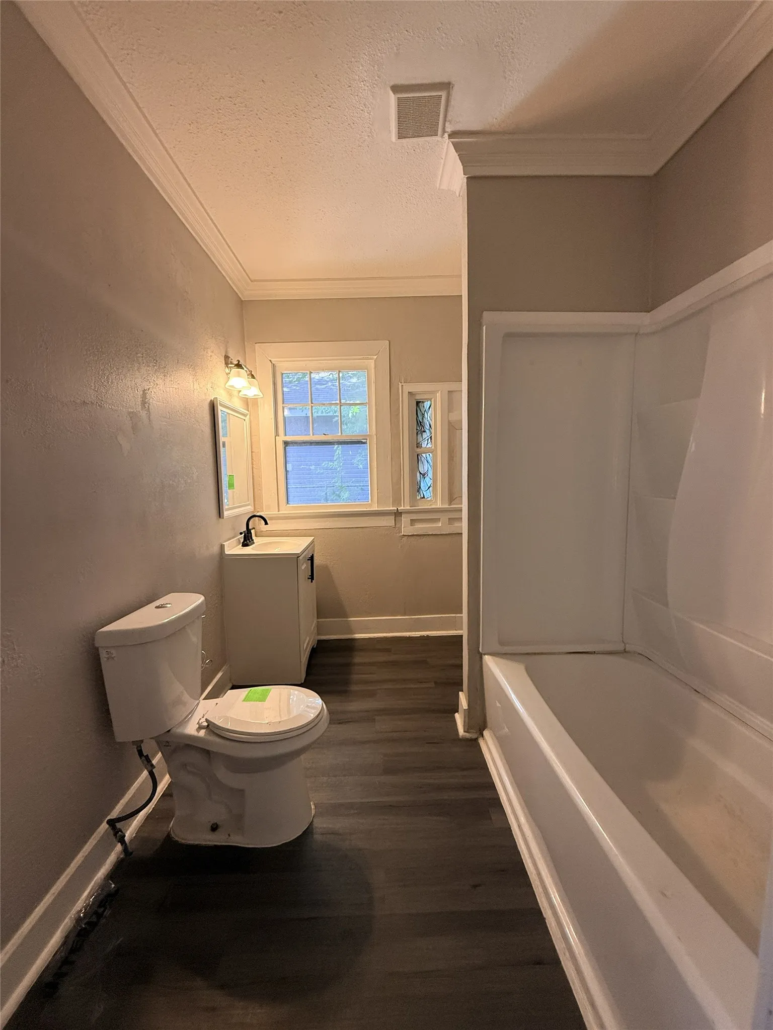 Wood-finish flooring, white vanity with black hardware, white tub, crown molding, and window with natural light