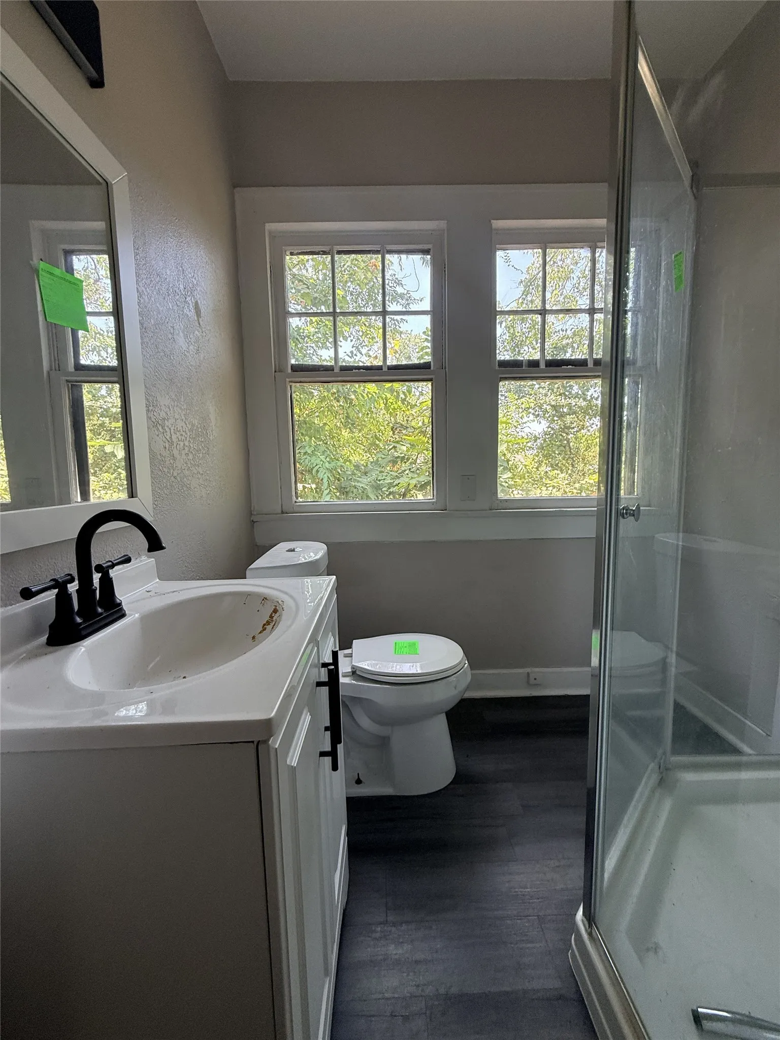 Bathroom featuring a white vanity with integrated sink, black fixtures, white toilet, and dark wood-finish flooring