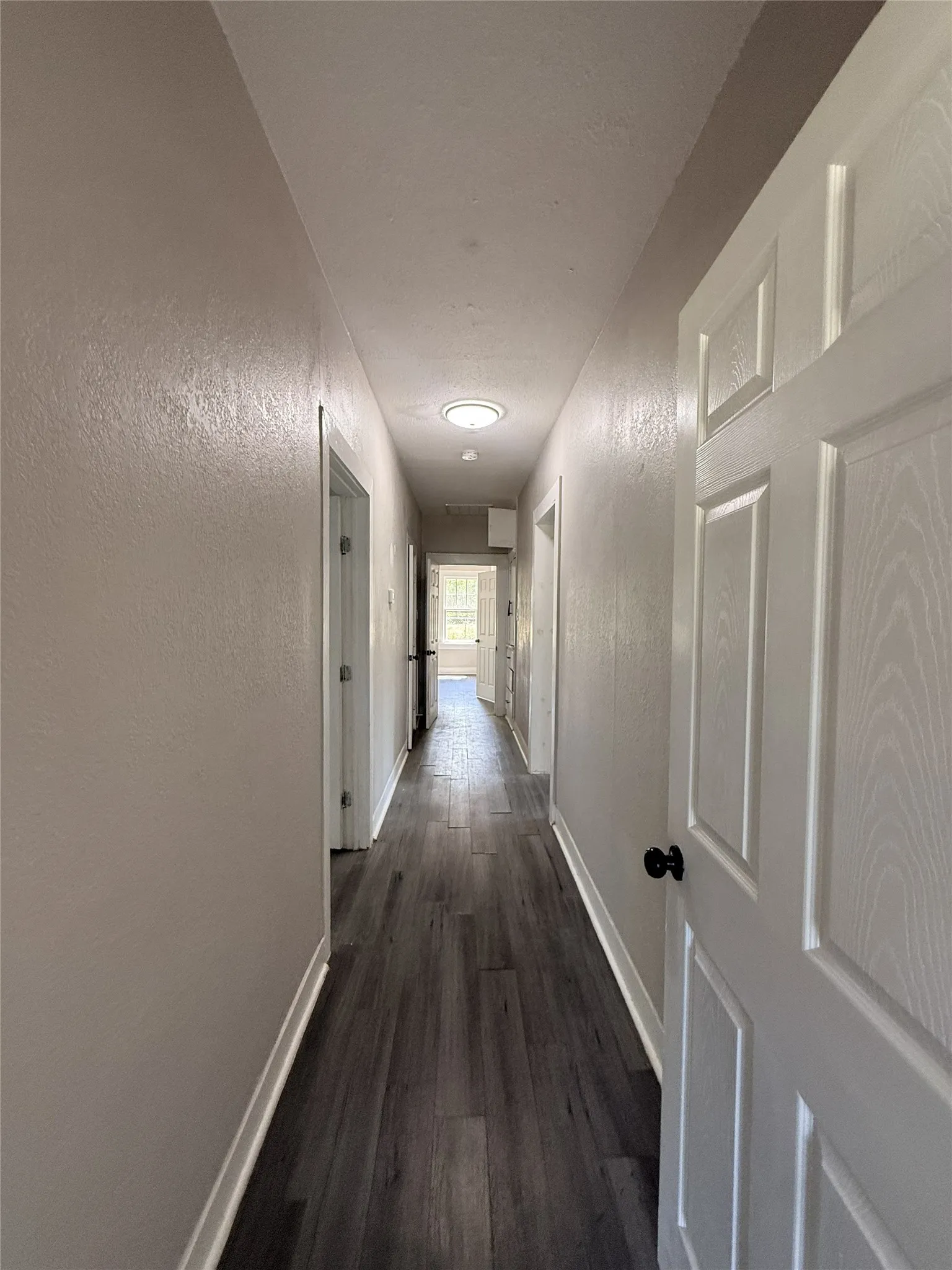 Hallway featuring wood-finish flooring, white panel doors with black hardware, and recessed lighting