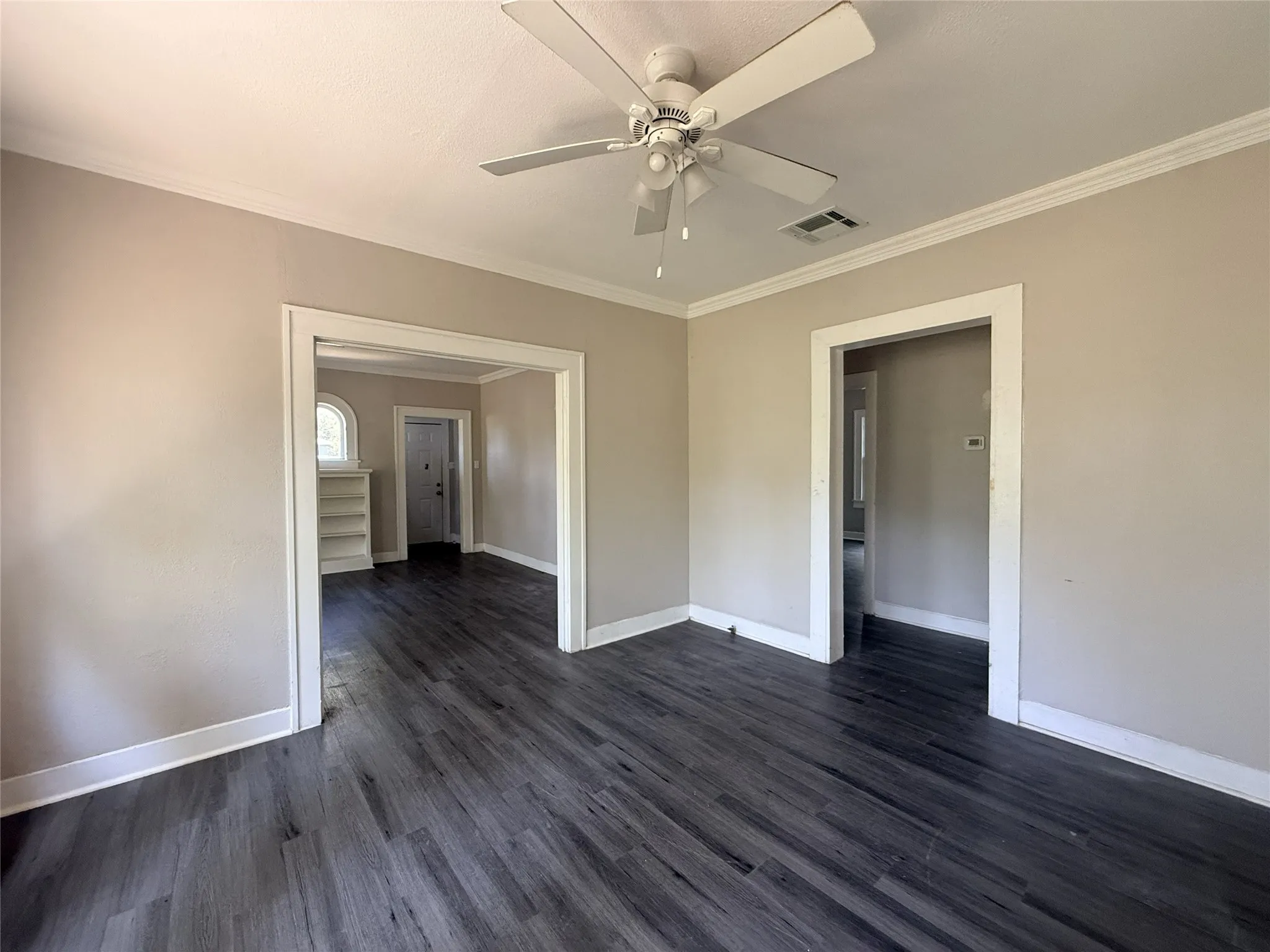 Wood-finish flooring, neutral wall paint, crown molding, and a ceiling fan with light fixture