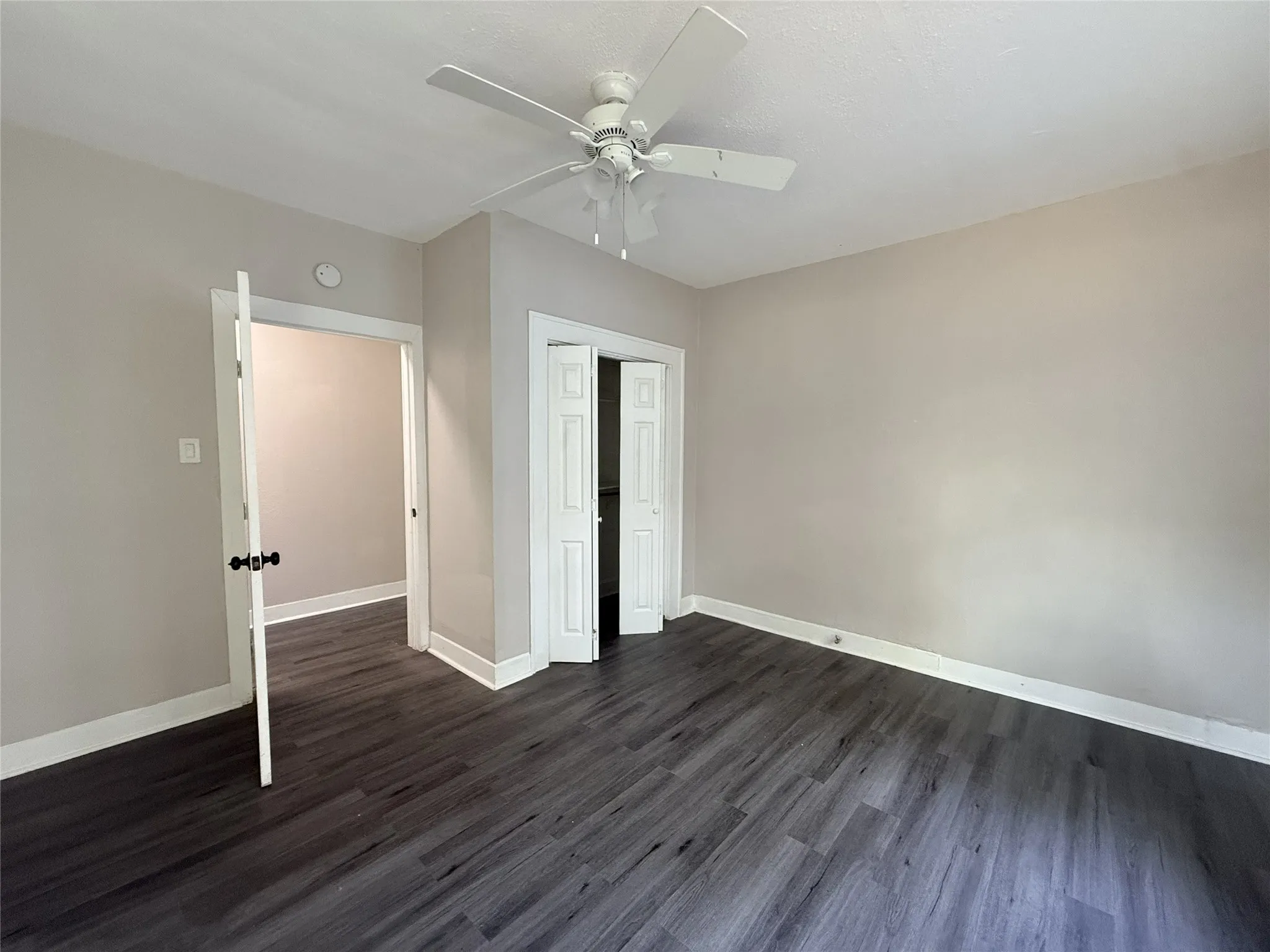 Wood-finish flooring, white trim, neutral wall color, ceiling fan, and white doors