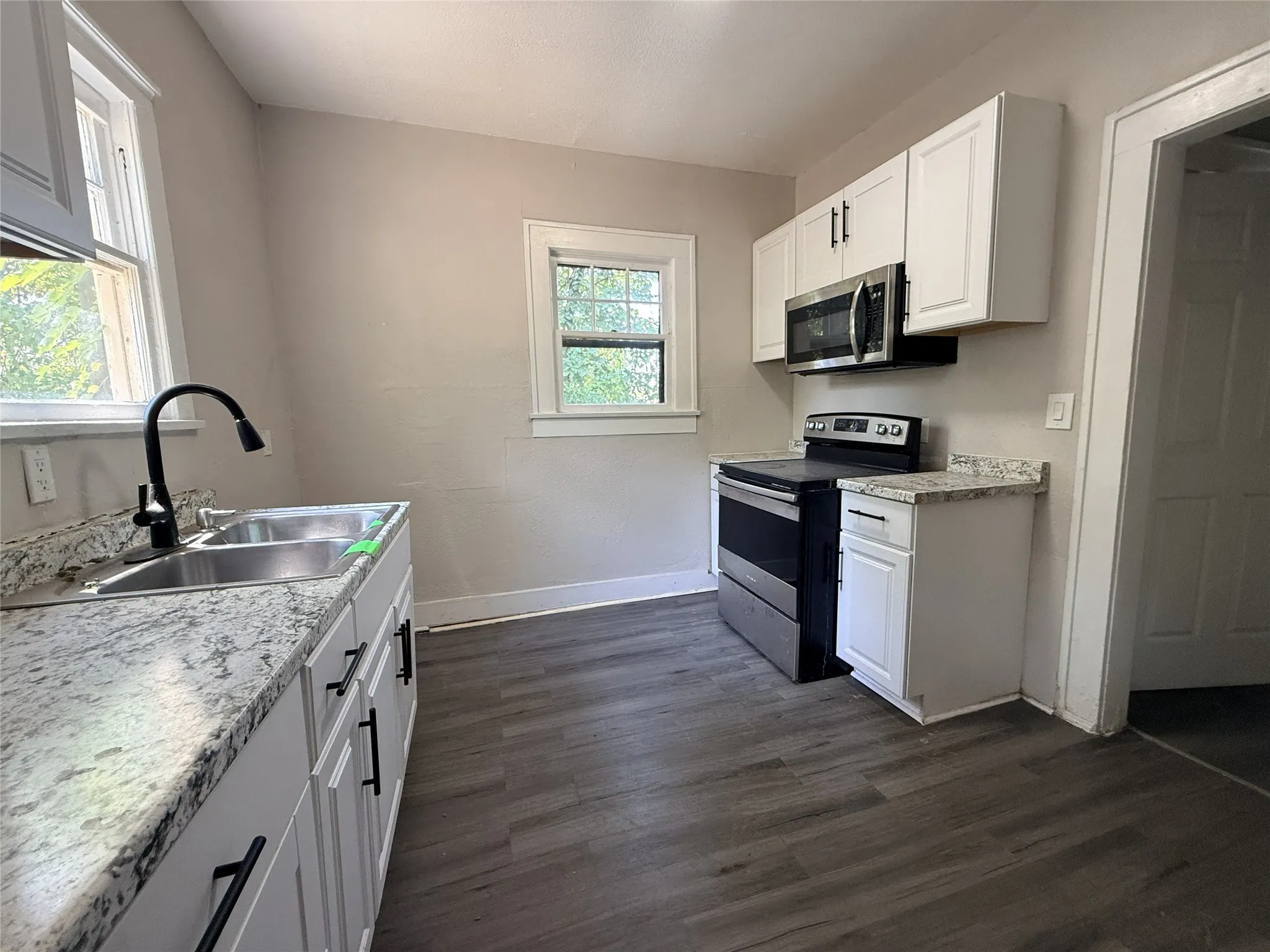 Kitchen featuring white cabinetry, stone-finish countertops, stainless steel sink with a matte black faucet, wood-finish flooring, and a stainless steel oven with an above-range microwave