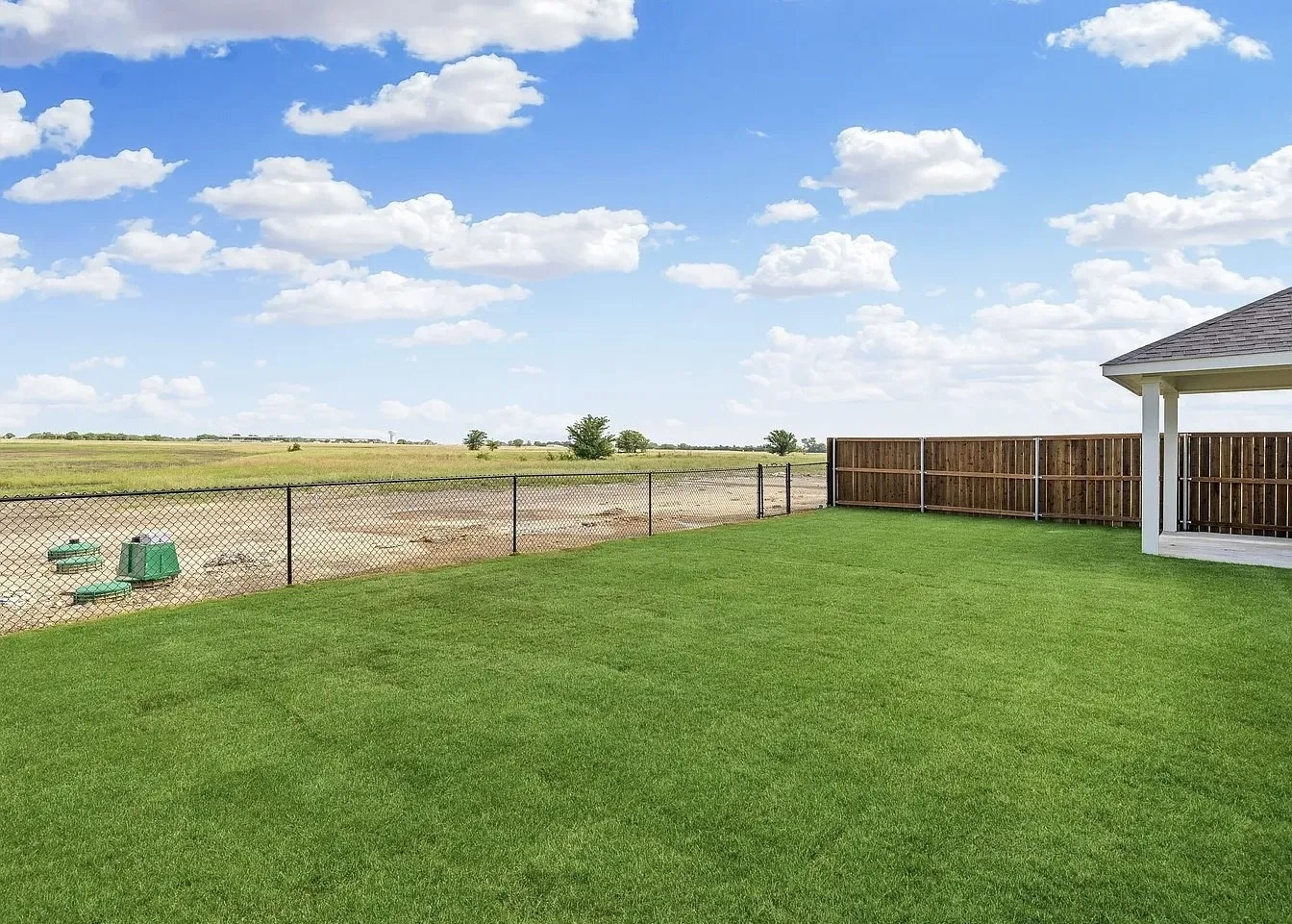 Expansive backyard featuring a manicured lawn, partial wood privacy fencing, and a partial chain-link fence