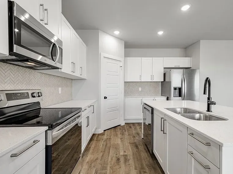 Kitchen featuring white cabinetry, stainless steel appliances, a herringbone tile backsplash, wood-finish flooring, and recessed lighting
