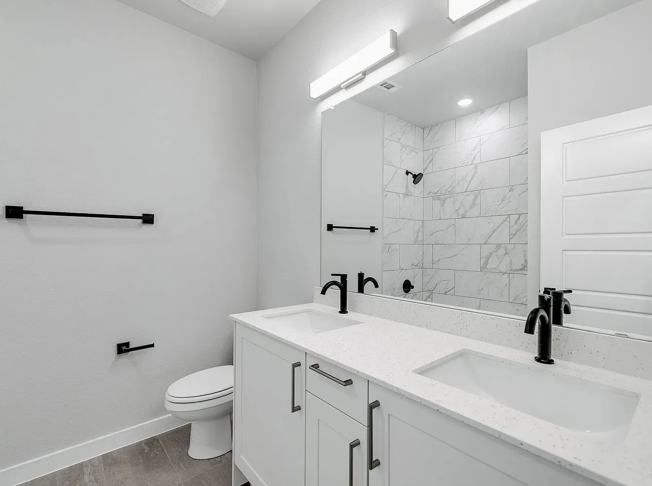 Dual vanity with white cabinetry and integrated sinks, matte black fixtures, full-width mirror, and tiled shower surround