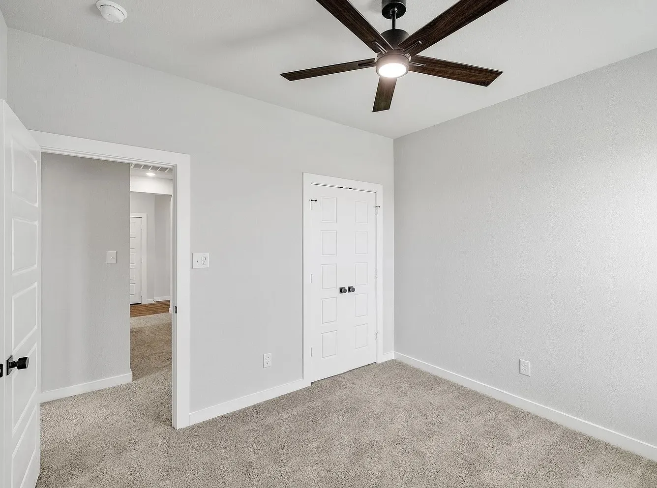 Carpeted flooring, white trim, paneled doors, and a ceiling fan with integrated lighting