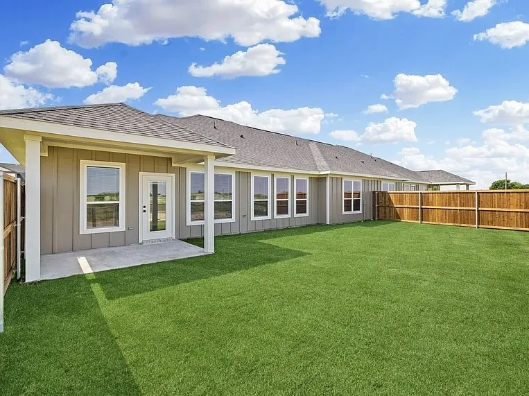Expansive rear lawn, covered patio, multiple windows, full-lite glass door, and privacy fencing