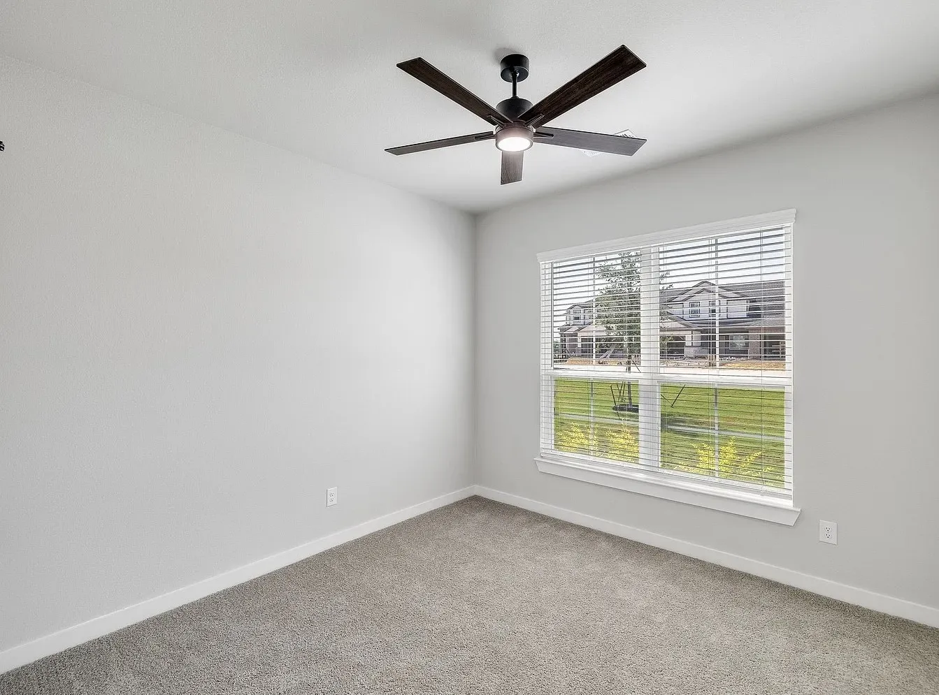 Neutral-toned walls, gray carpeting, window with horizontal blinds, and a dark-bladed ceiling fan with integrated lighting