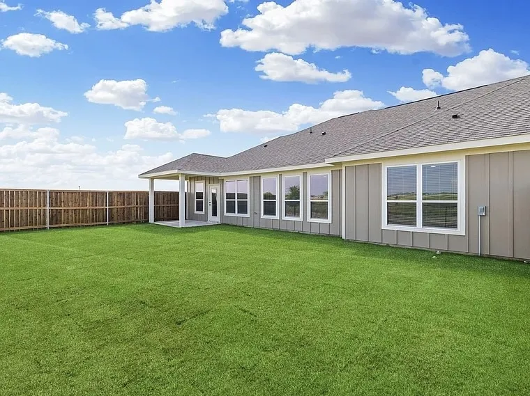 Expansive backyard with a covered patio, wood privacy fencing, and a manicured lawn
