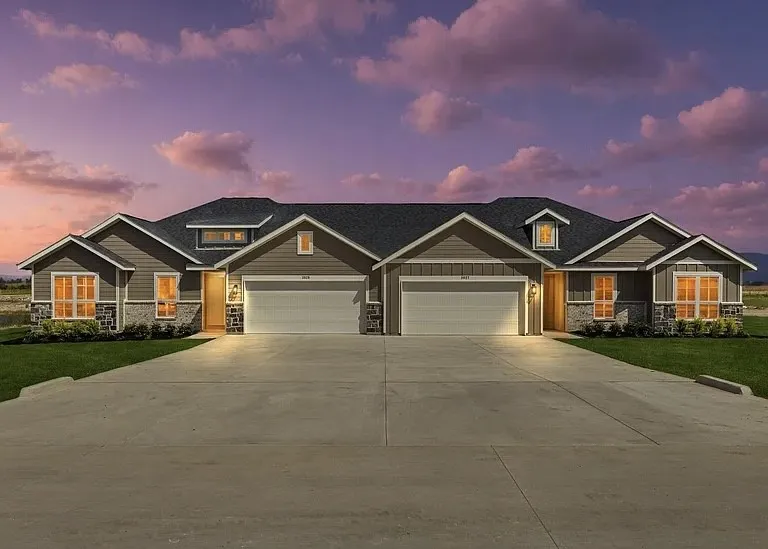 Duplex residence featuring a pitched shingle roof, dormer windows, horizontal siding, and stone veneer accents