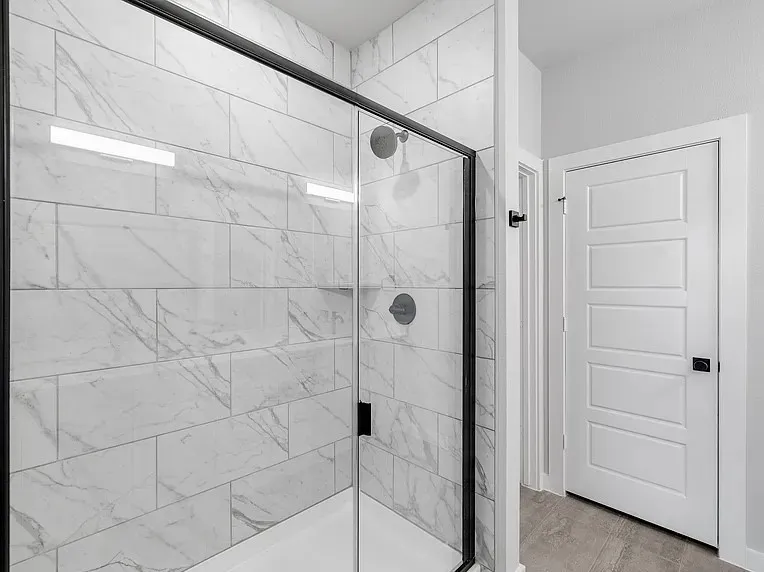 Shower enclosure with a frameless glass panel, matte black fixtures, and white subway tile surround