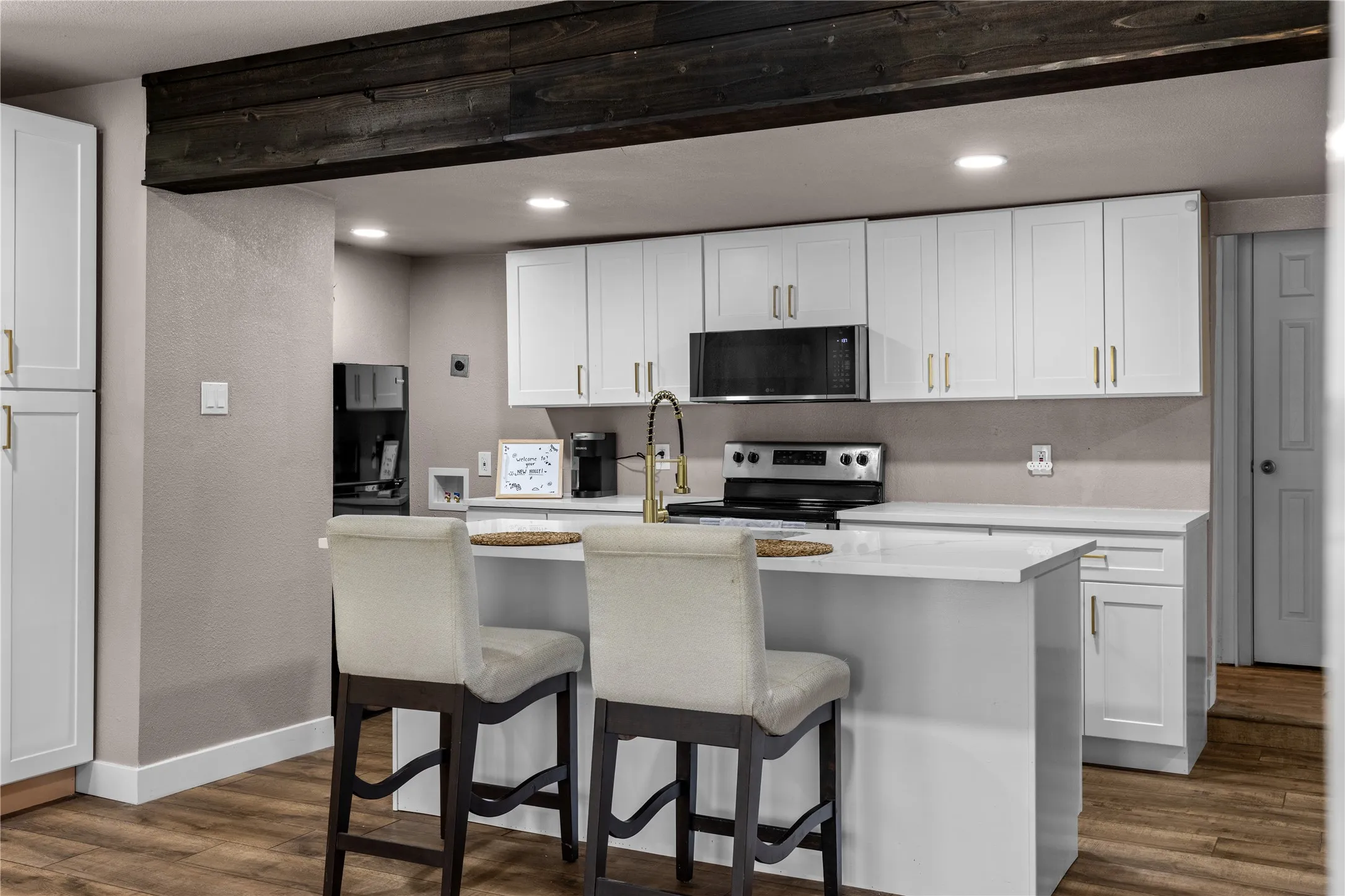 Kitchen featuring white cabinetry with gold-toned hardware, an integrated kitchen island with seating, a stainless steel range, and a microwave