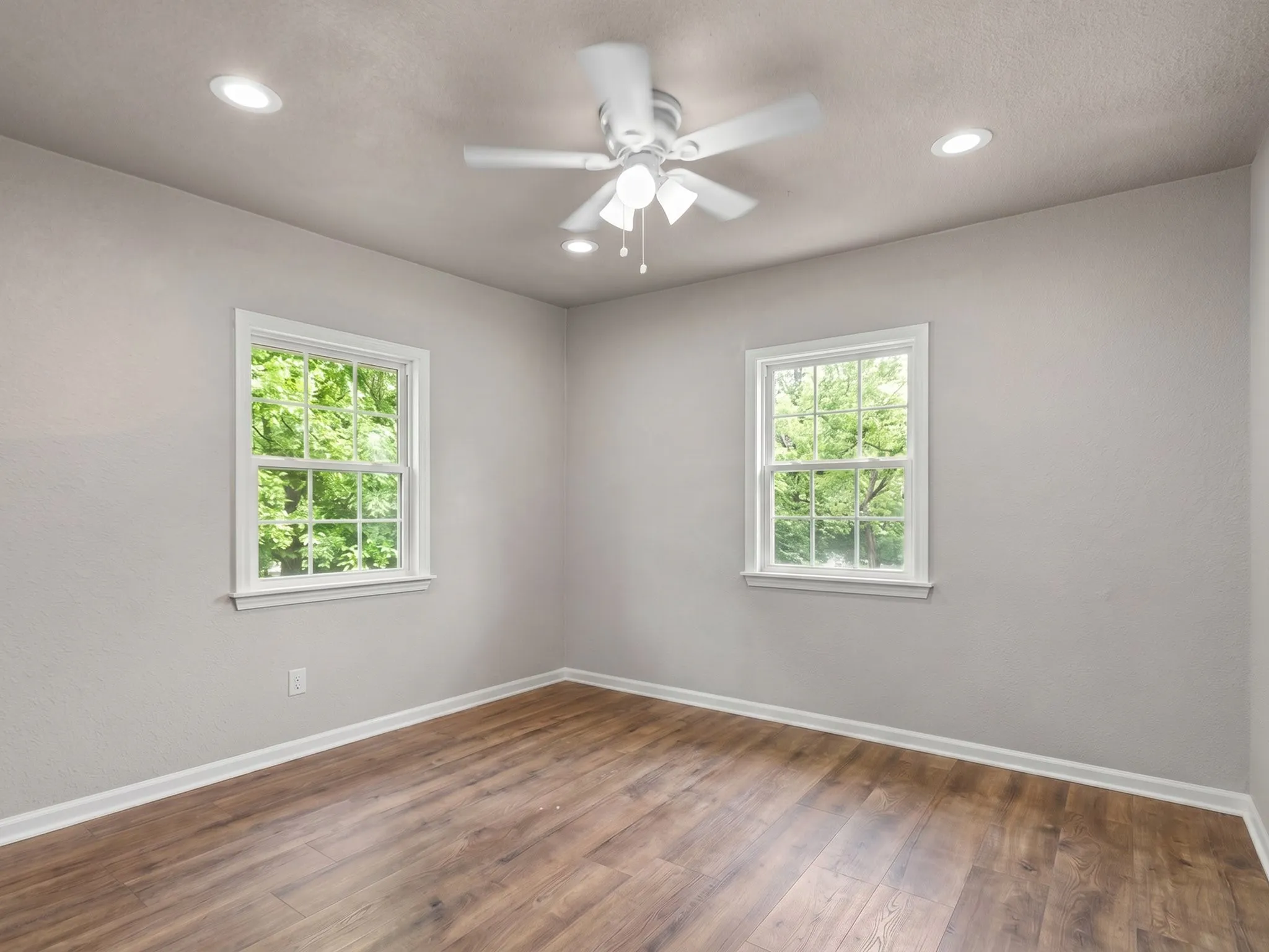 Wood-finish flooring, dual windows with white trim, recessed lighting, and a white ceiling fan with integrated lighting