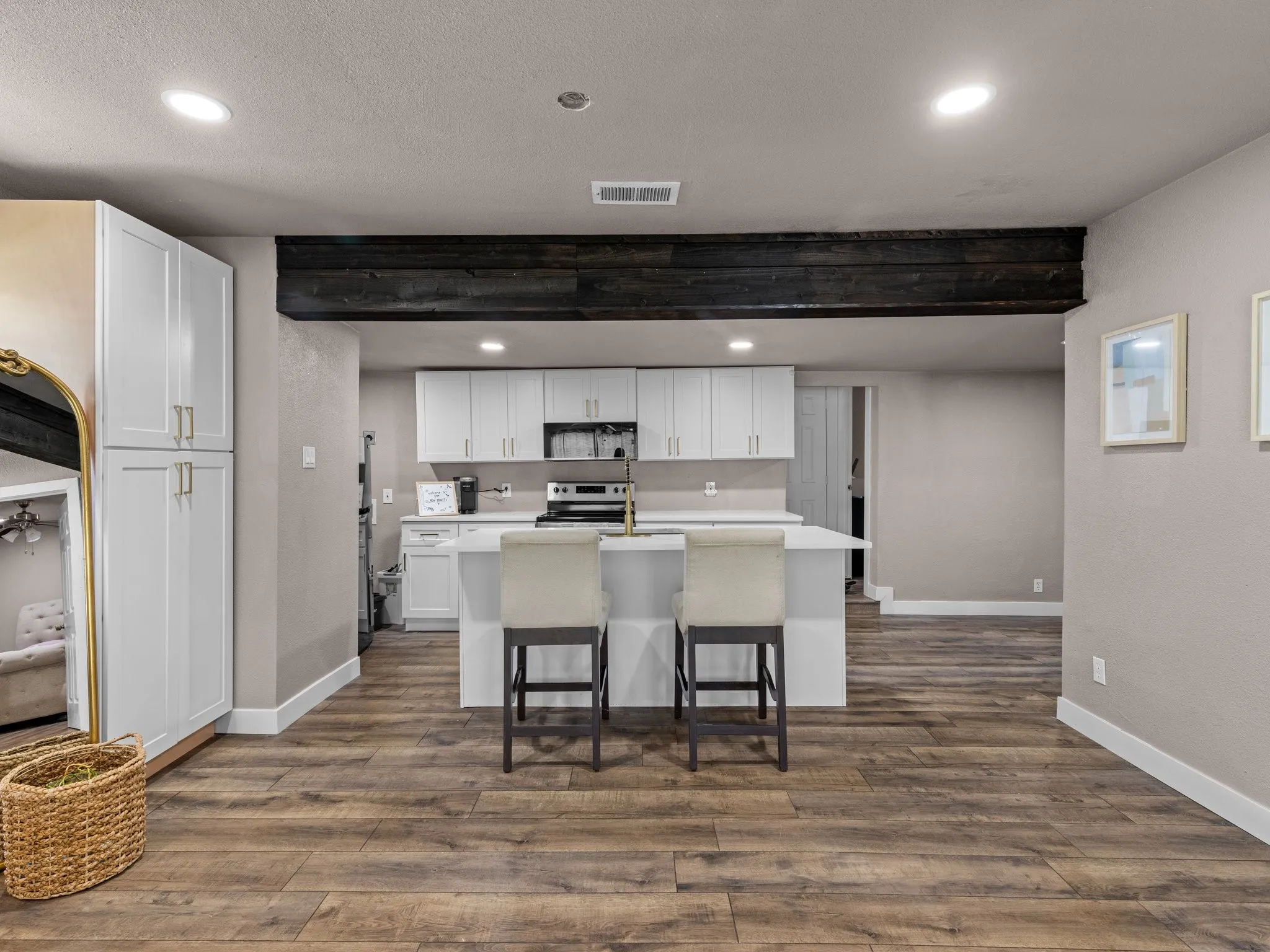 Wood-finish flooring, recessed lighting, white cabinetry with gold-finish hardware, kitchen island with counter seating, and a dark exposed ceiling beam