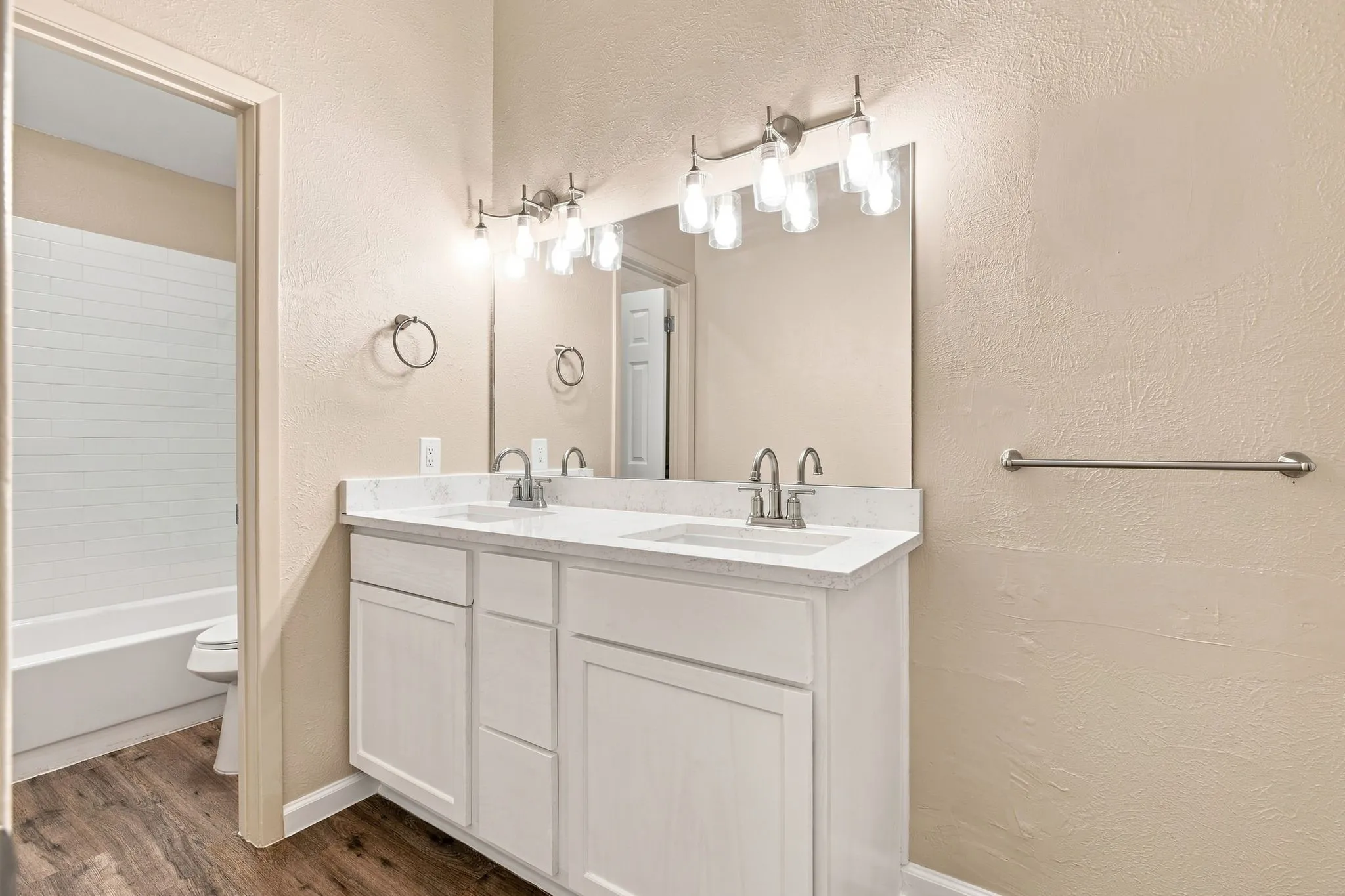 Double vanity with white cabinetry, light-toned countertop, dual sinks with brushed nickel fixtures, and twin multi-bulb light fixtures
