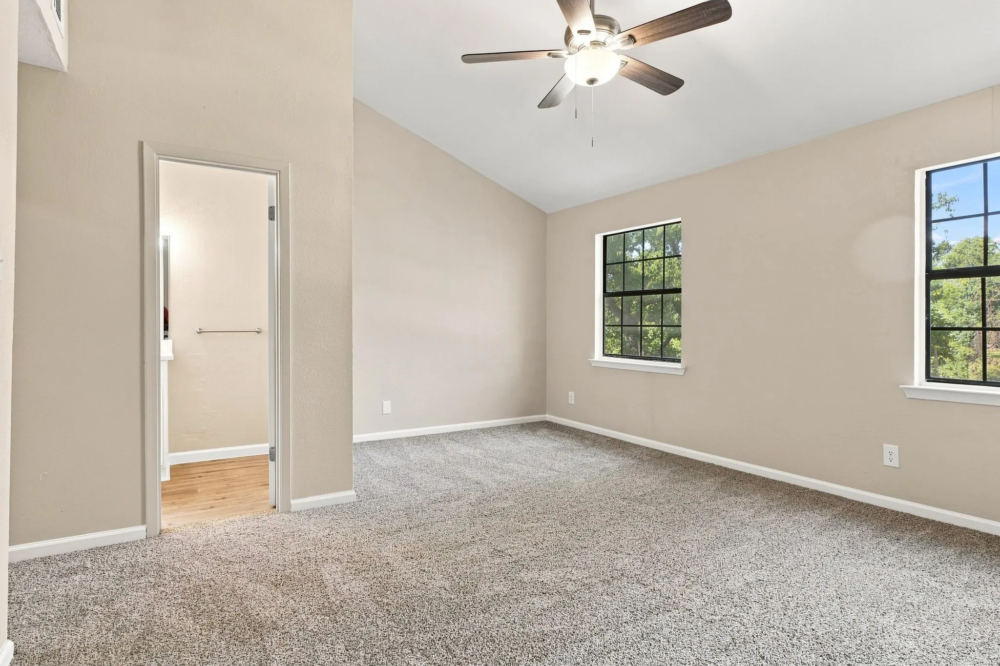 Vaulted ceiling with an integrated ceiling fan, two large windows, and neutral carpeting