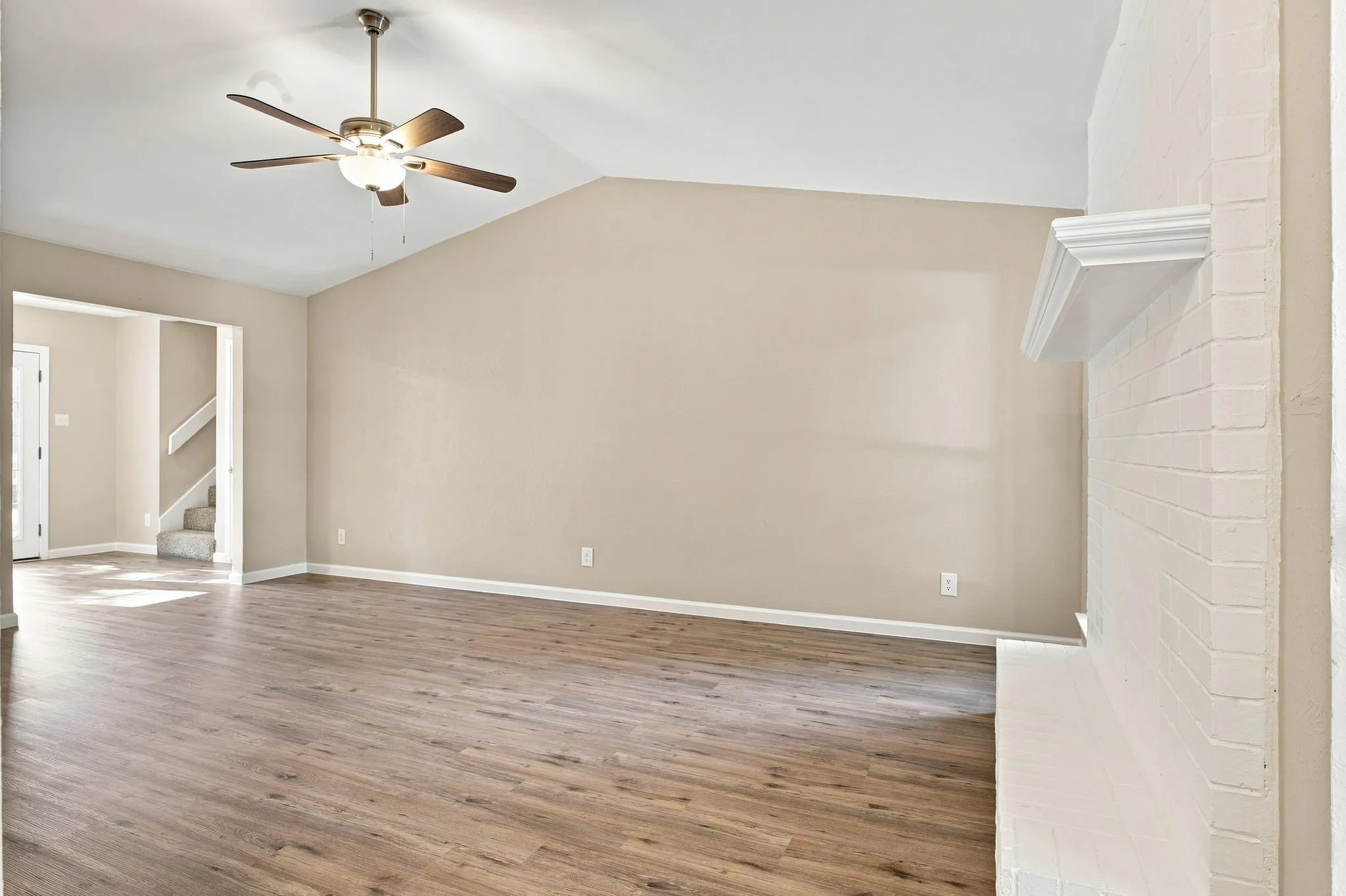 Vaulted ceiling with ceiling fan, wood-finish flooring, white brick fireplace, and multiple windows
