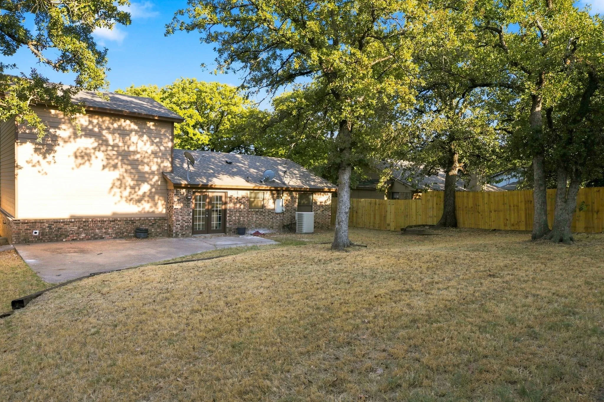 Expansive backyard featuring mature trees, a concrete patio, and a newly installed wood privacy fence