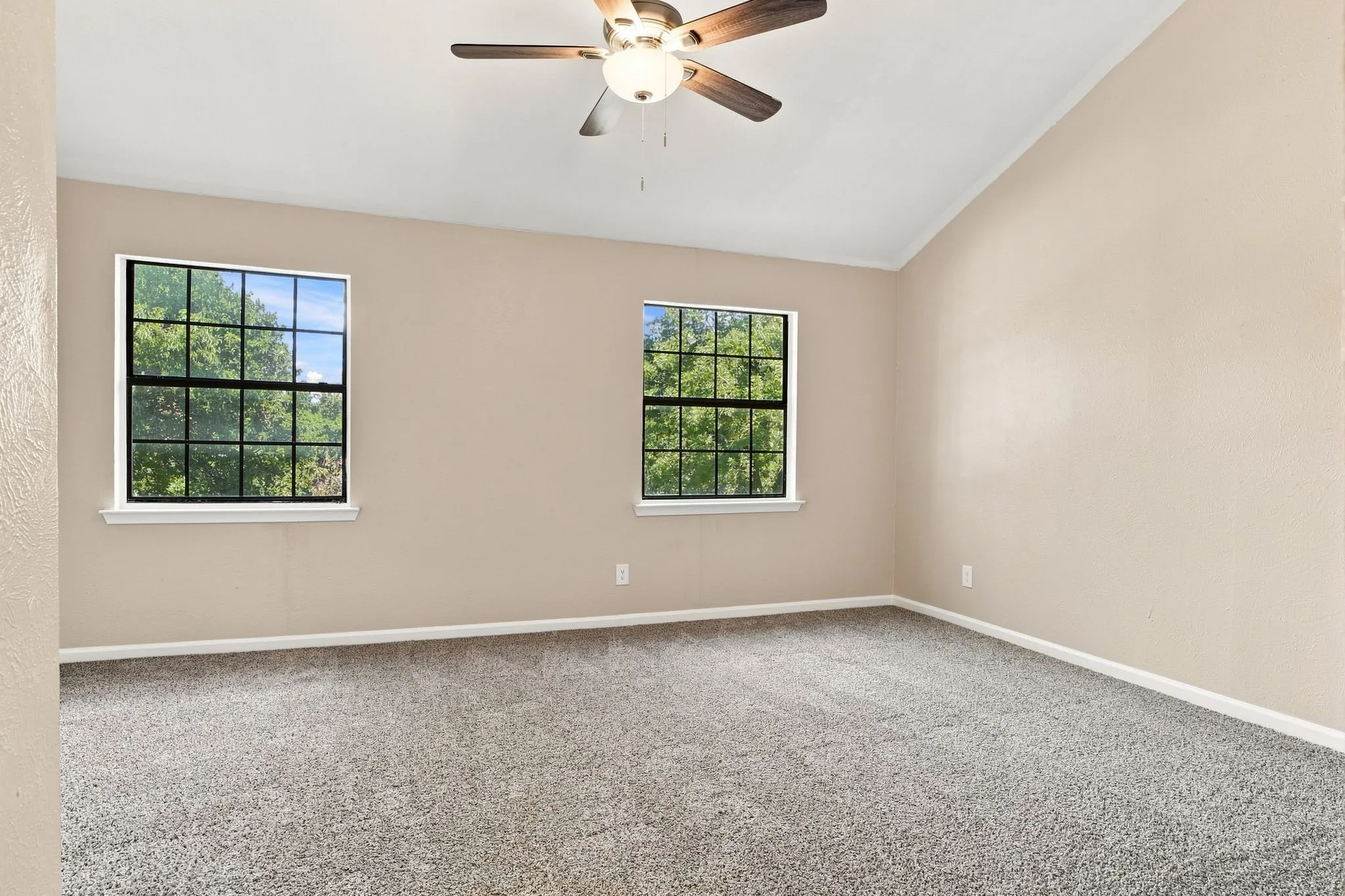 Vaulted ceiling, two large windows, ceiling fan, and grey carpet flooring