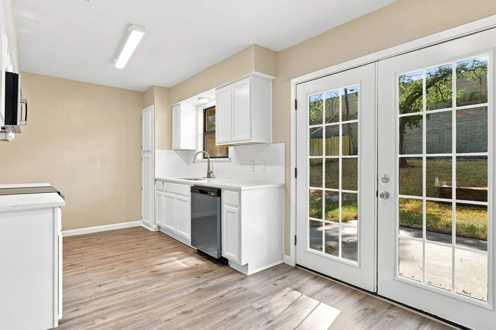 White cabinetry with brushed nickel hardware, stainless steel dishwasher, wood-finish flooring, white subway tile backsplash, and double glass-paneled doors