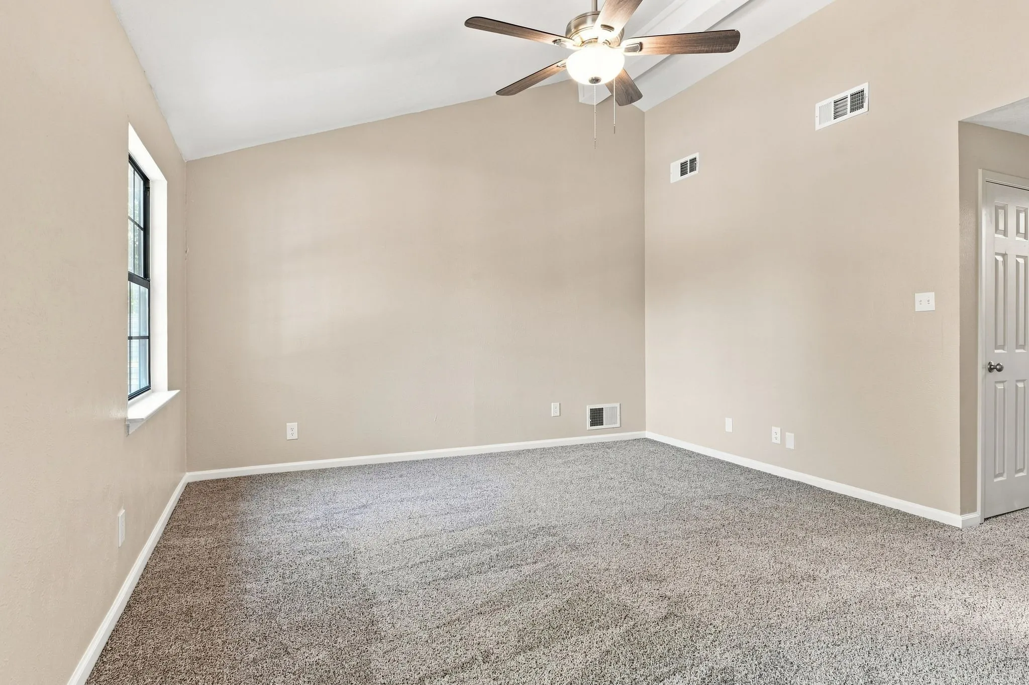 Vaulted ceiling with an attached ceiling fan, neutral wall paint, gray carpeting, and a multi-pane window
