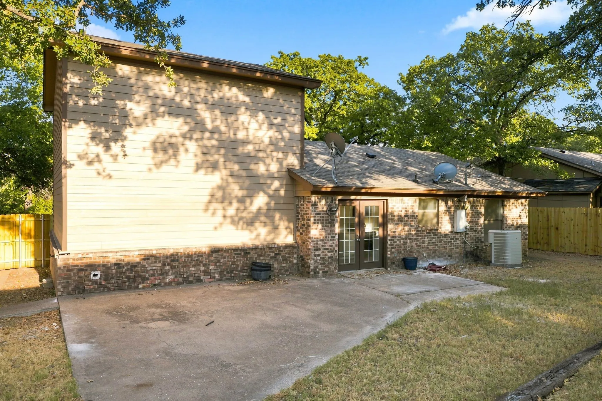 Rear exterior featuring a brick and siding facade, concrete patio, double glass-paned doors, and exterior lighting