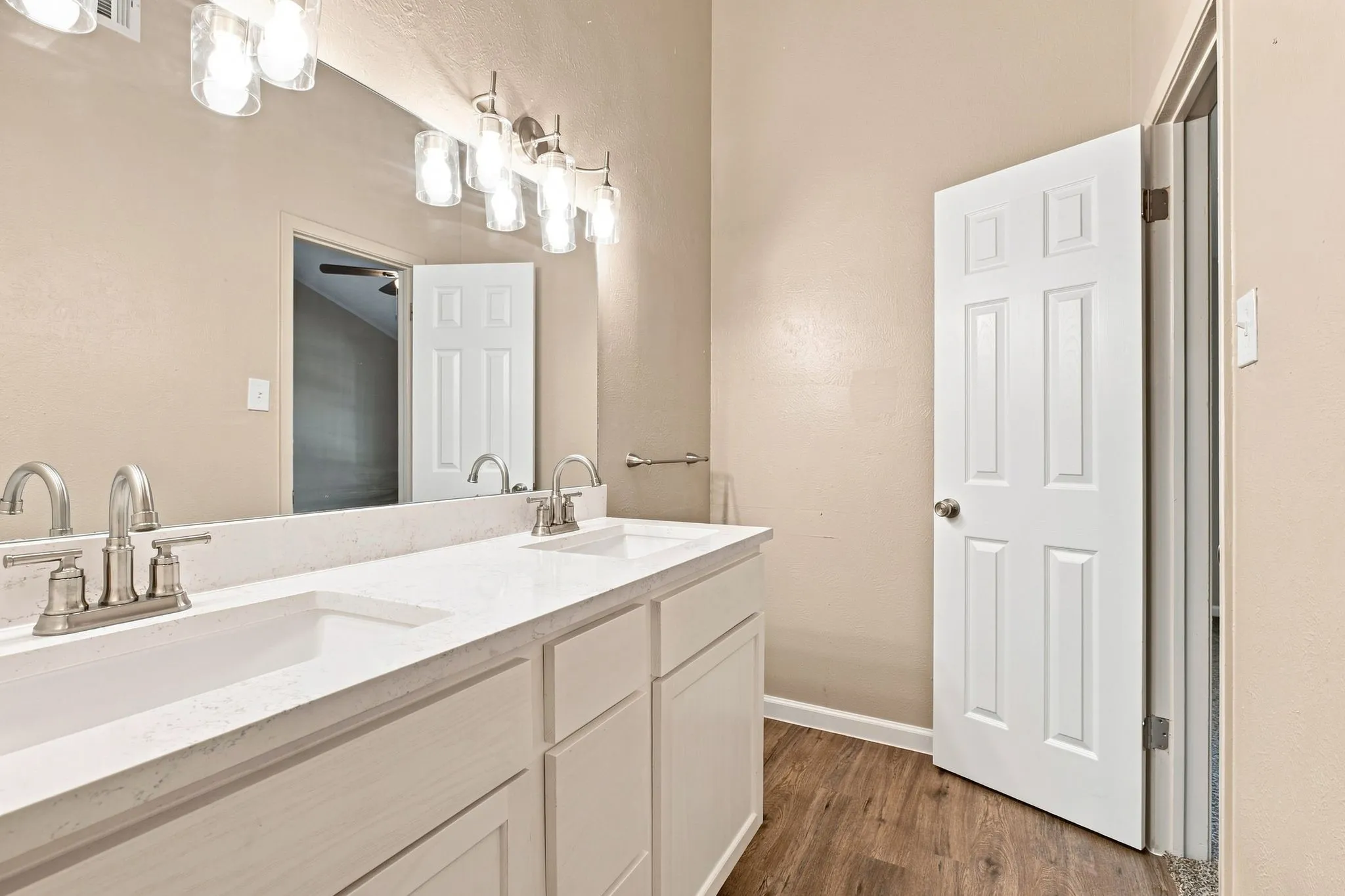 Dual undermount sinks, expansive vanity with white cabinetry, wood-finish flooring, and brushed nickel fixtures