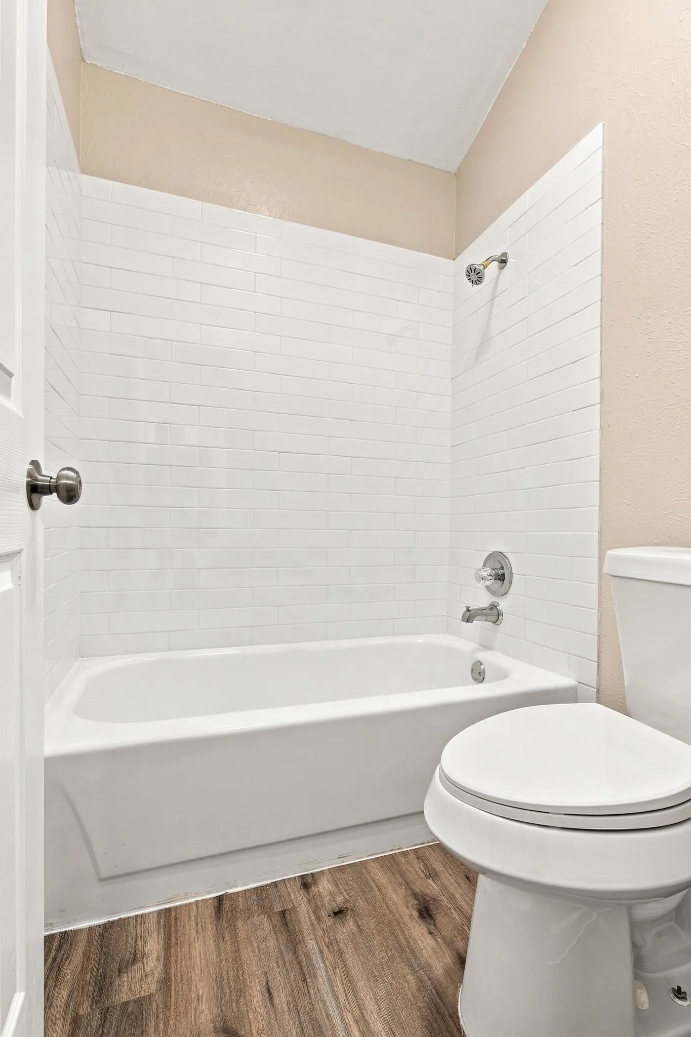 Bathtub with subway tile surround, chrome fixtures, and wood-finish flooring