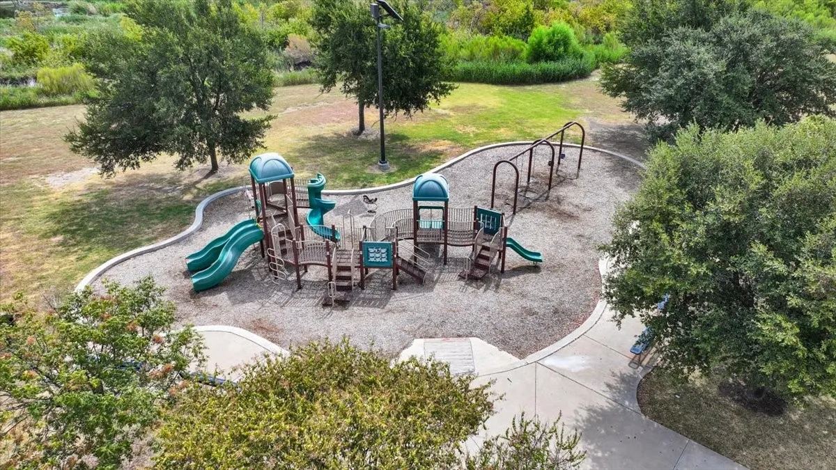 Community playground featuring multi-level play structures with slides, climbing components, and metal arch bars, set within a rubberized safety surface