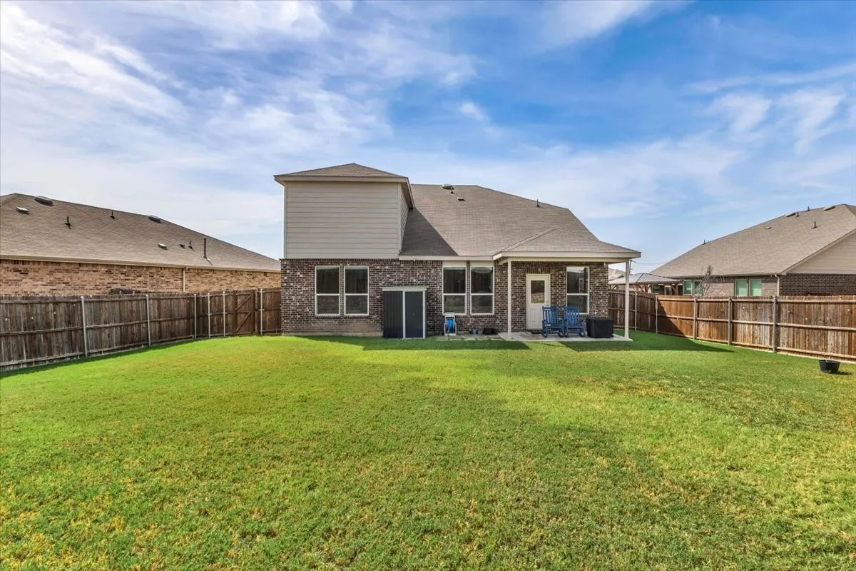 Expansive lawn with wood privacy fencing, covered patio, and brick exterior