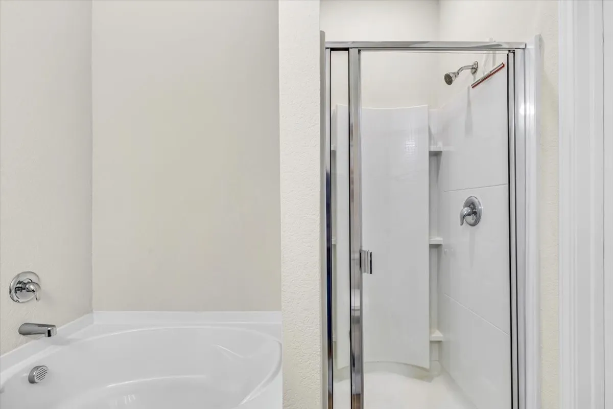 Built-in bathtub with polished chrome fixtures and an adjacent standing shower with clear glass enclosure and chrome hardware