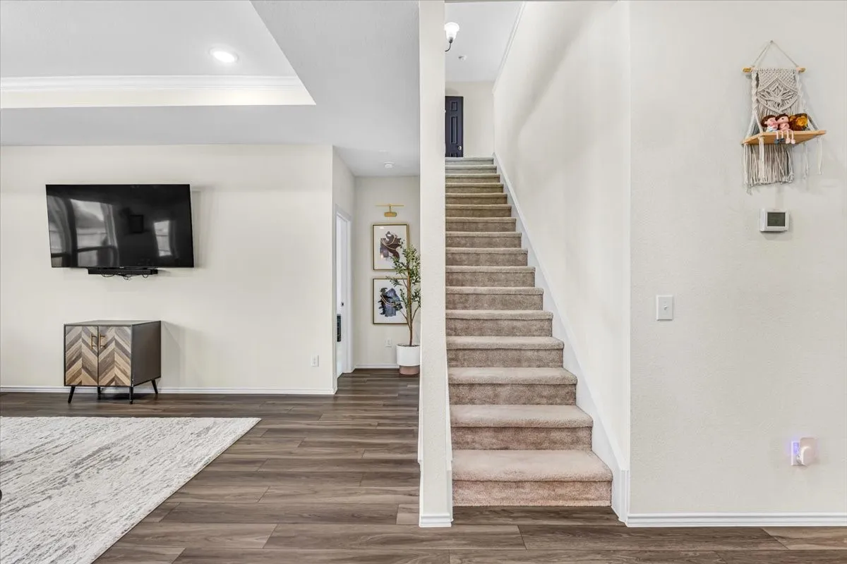 Tray ceiling with recessed lighting, wood-finish flooring, carpeted staircase, and white wall finishes