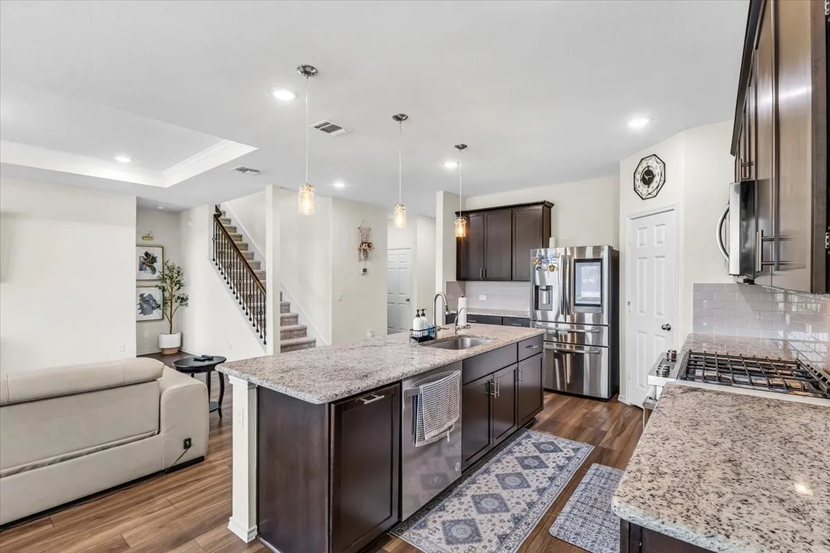 Open-concept kitchen featuring granite countertops, dark wood-finish cabinetry, stainless steel appliances, and a central island with an integrated sink