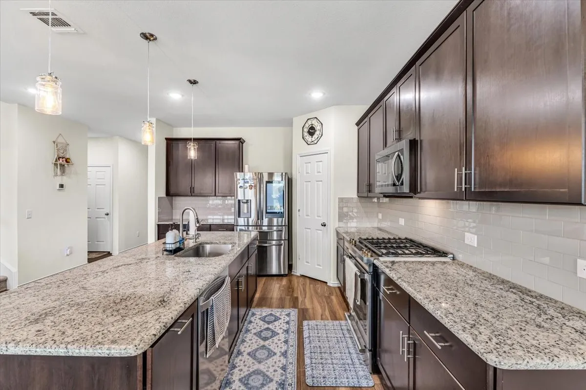 Kitchen featuring a gas range, stainless steel appliances, dark wood-finish cabinetry, light-toned countertops, and a white subway tile backsplash