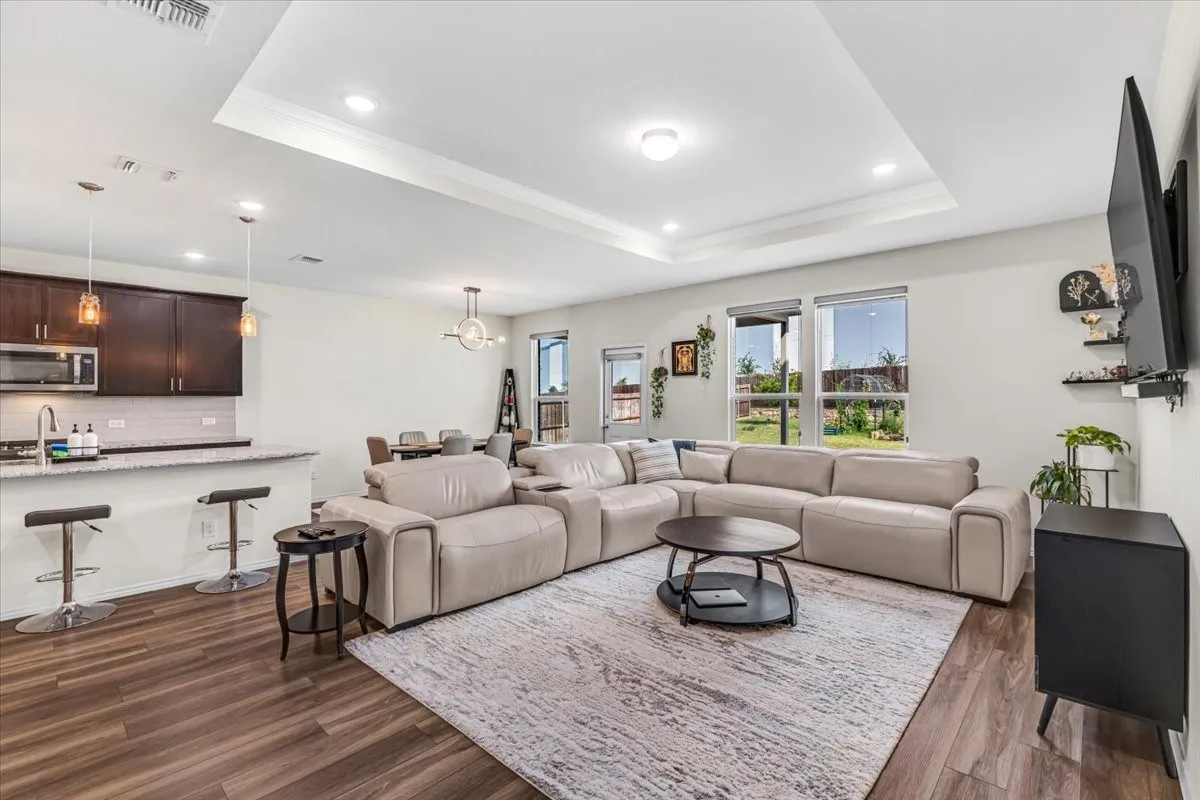 Open concept living area with wood-finish flooring, recessed lighting, and a tray ceiling