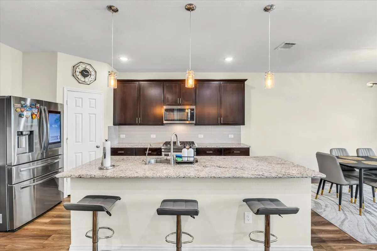 Kitchen island with a light-toned countertop, stainless steel appliances, dark wood cabinetry, tile backsplash, and wood-finish flooring