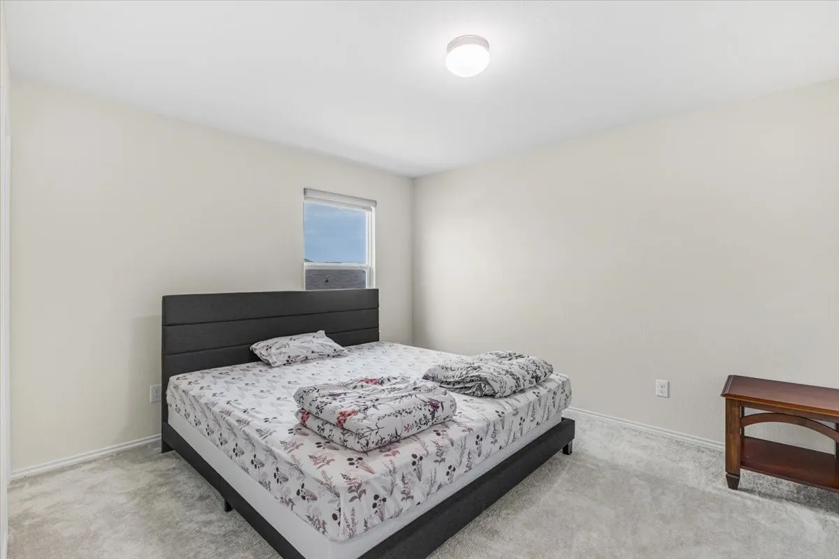Spacious bedroom featuring a black upholstered bed frame, neutral wall finishes, recessed ceiling lighting, carpet flooring, and a window with natural light exposure