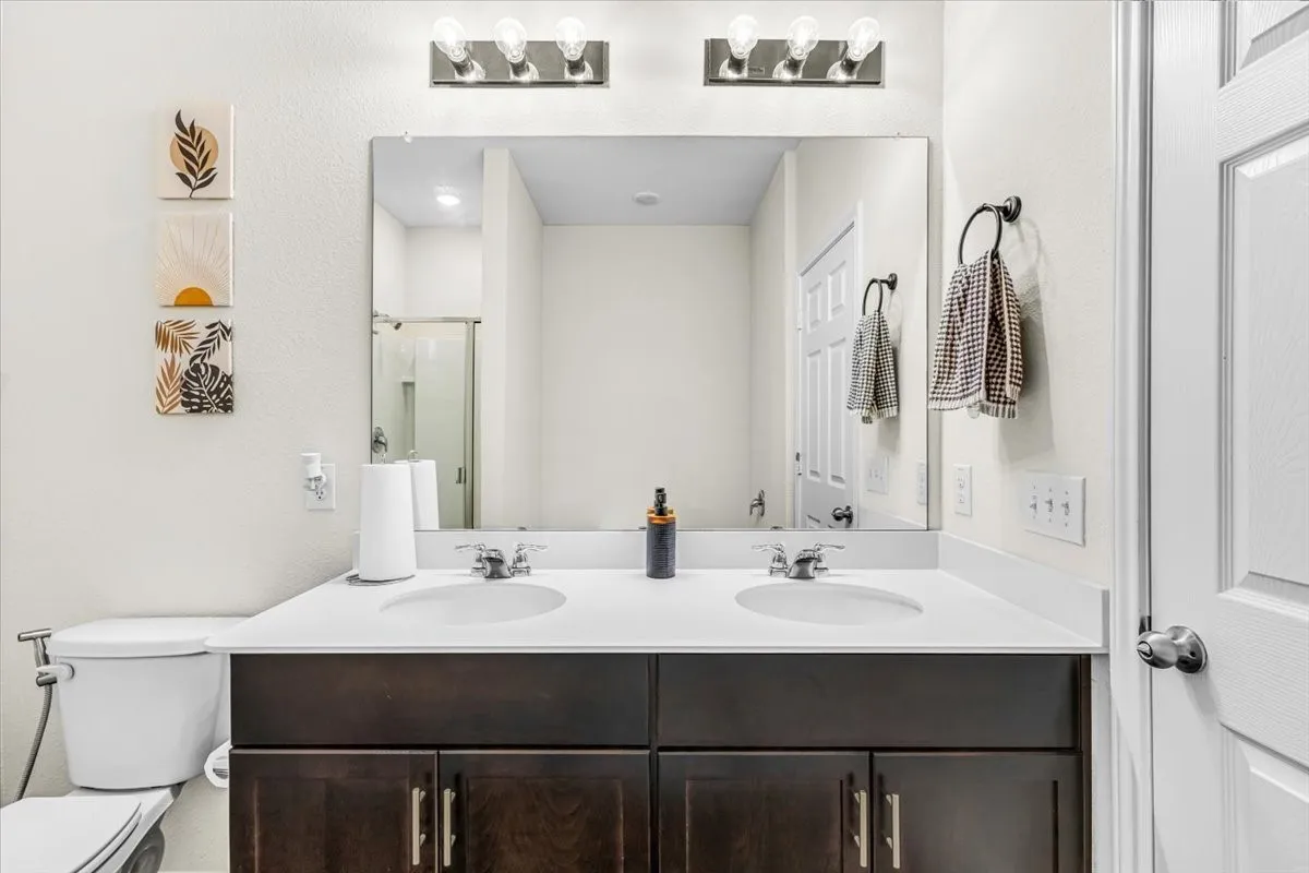 Dual-sink vanity featuring a dark wood-finish cabinet base with brushed metal hardware, white quartz countertop, and chrome faucets