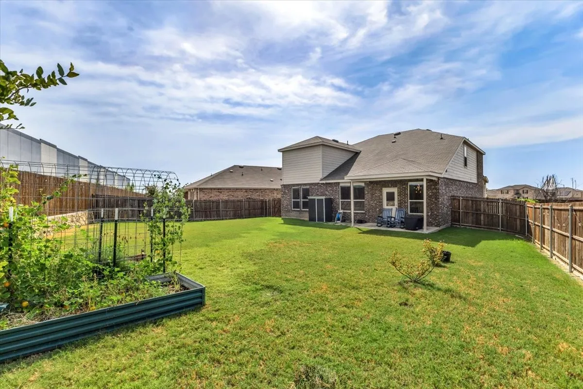 Expansive backyard featuring a manicured lawn, wood fencing, and a raised garden bed