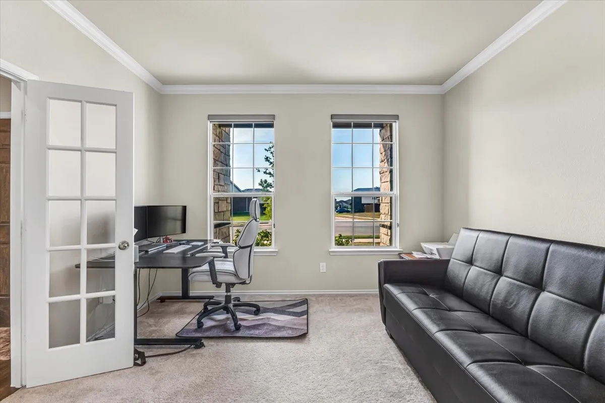 Room featuring French doors with glass panes, two windows with blinds, crown molding, and neutral-toned wall paint