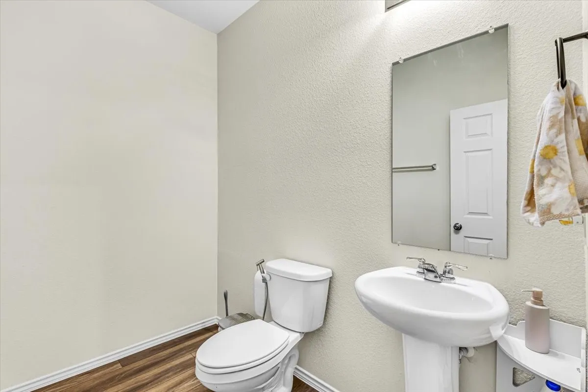 Pedestal sink with chrome faucet, wall-mounted rectangular mirror, and wood-finish flooring