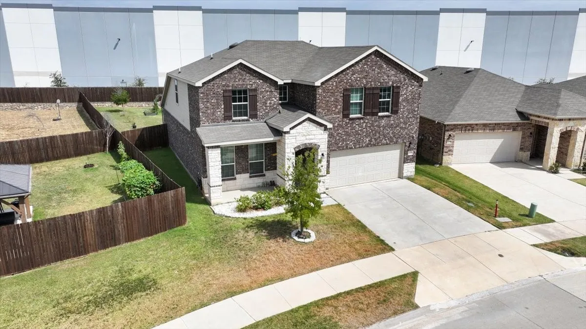 Two-story residence featuring a brick and stone facade, attached two-car garage, and a fenced backyard