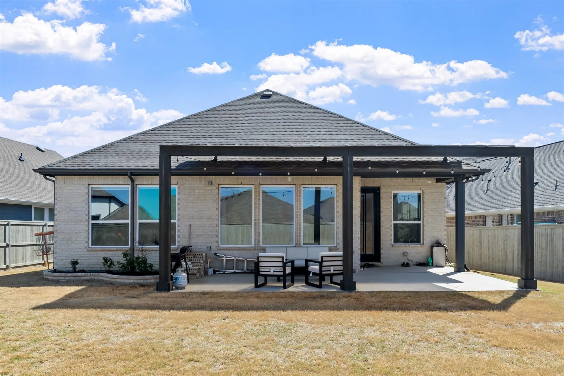 Expansive backyard featuring a pergola over a concrete patio, brick exterior, and multiple windows