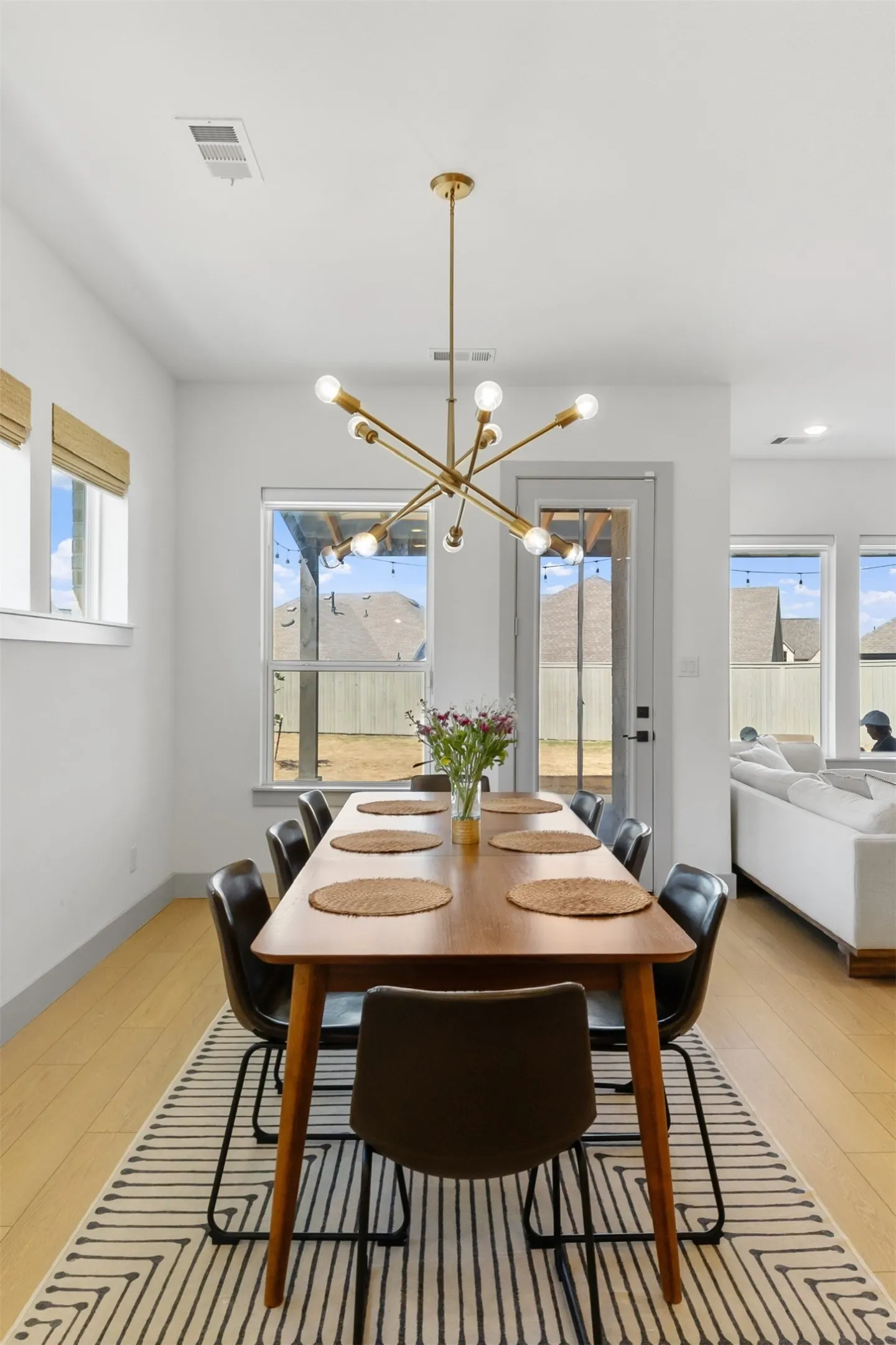 Bright interior space with wood-finish flooring, a contemporary gold-finish chandelier, and multiple large windows